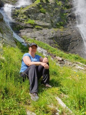 Nadja von klimafit-ing sitzend auf einer Wiese vor einem Wasserfall.